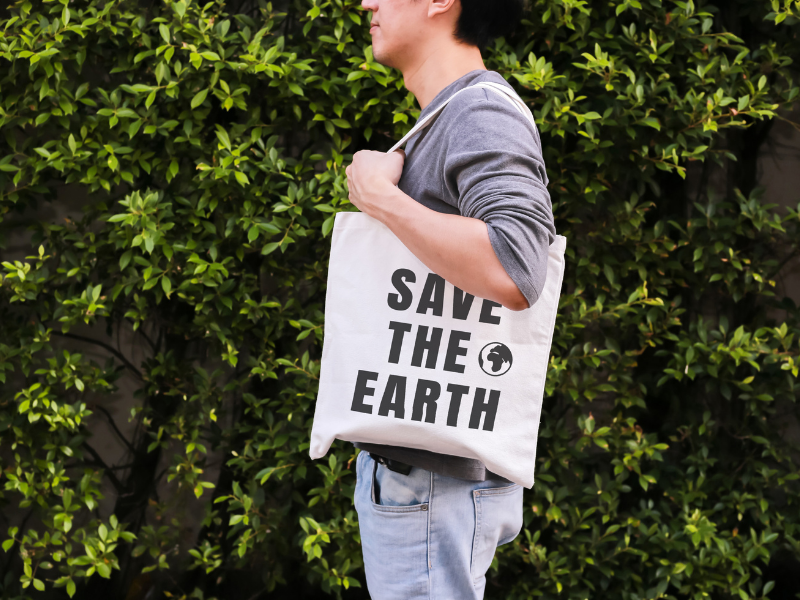 Uomo con shopping bag a tracolla in tela bianca con scritta "Save the Earth" nera