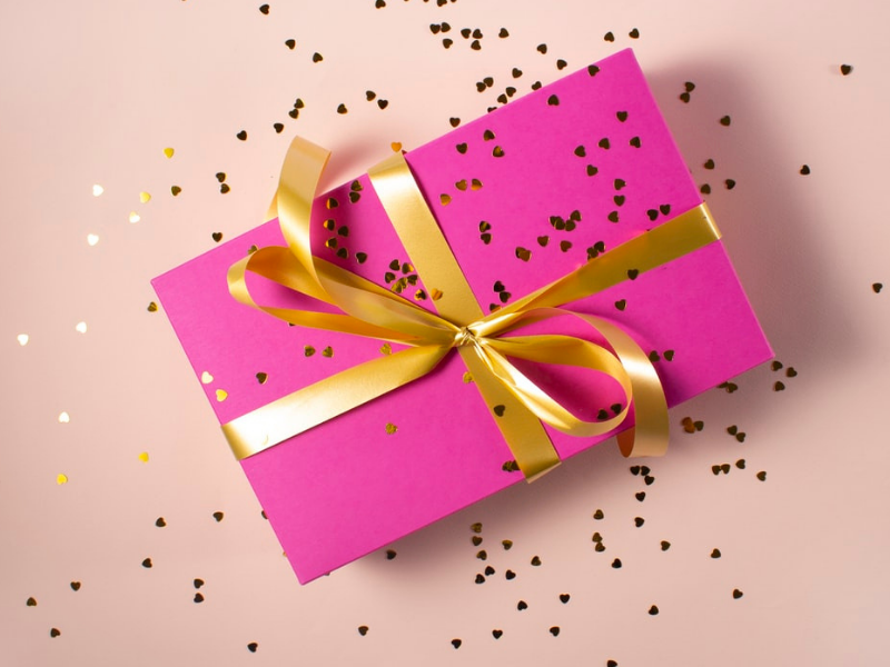 Pacco regalo con carta rosa e fiocco dorato